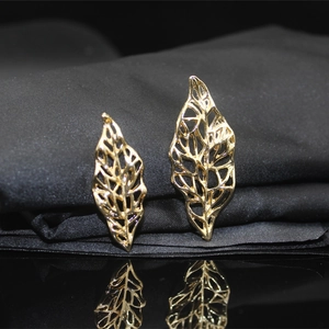 Macro shot of gold hollow leaf earrings on black silk with a clear mirror reflection
