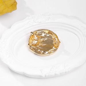 Back view of sun goddess golden metal brooch with irregular texture on a white tray