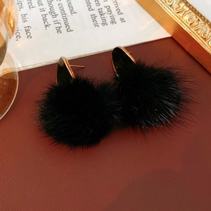 Detail of twisted oval gold earrings with black fur pom pom on red leather