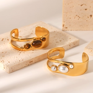 Detailed view of wide open gold bangles with natural tiger eye and white pearl accents