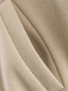 Detailed macro view of the thick beige tweed fabric texture and pocket stitching of the jacket