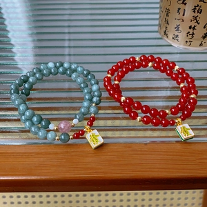 Detail of red agate and green beaded bracelets with lucky mahjong pendants on glass