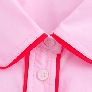 Dettaglio del colletto rosa con bordino rosso a contrasto e due bottoni bianchi