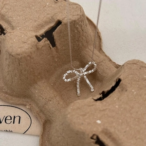 Close-up of a silver bow necklace pendant on a textured brown artistic paper background