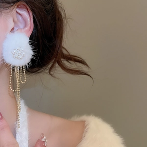 Detailed close-up of a long tassel earring with white fur balls and pearls on a model