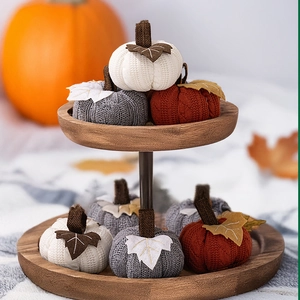 Three knitted decorative pumpkins in white, gray, and caramel colors on a wooden tray