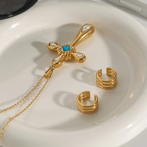 Detail view of gold cross pendant with blue zircon and matching ear cuffs in a ceramic tray