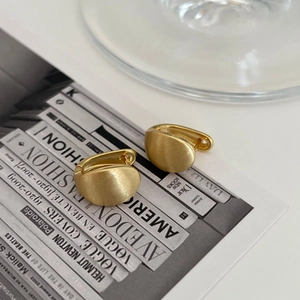 Matte gold irregular geometric stud earrings with brushed finish on a fashion magazine