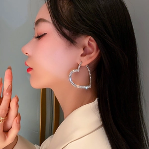 Vue latérale du mannequin portant de grandes boucles d'oreilles cœur argentées et strass