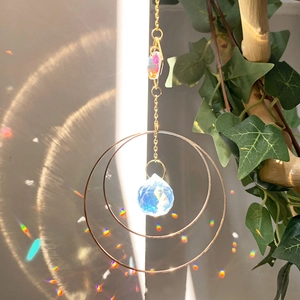Detail of sun catcher crystal sphere reflecting rainbow light on wall with ivy branch