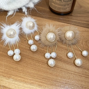 Detailed view of fur ball pearl tassel earrings on a rustic wood surface with warm lighting