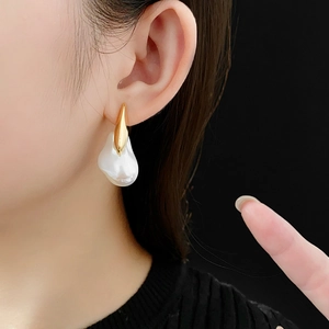 Detailed view of an irregular white pearl earring with gold-plated finish on a female model