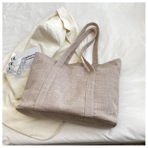 Minimalist khaki canvas tote bag styled on white fabric with a chic blazer backdrop