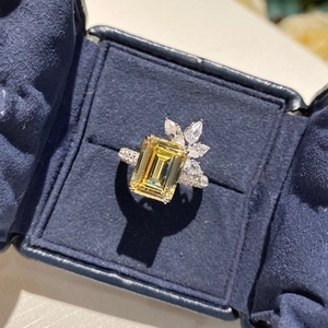 Macro shot of yellow emerald-cut gemstone ring with floral diamond accents in velvet box