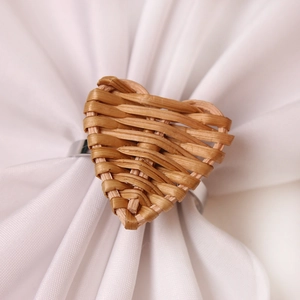 Handwoven rattan heart napkin ring with silver metal base on white linen fabric
