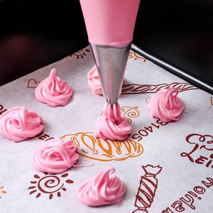 Gros plan d'une poche à douille jetable pressant du glaçage rose sur du papier cuisson
