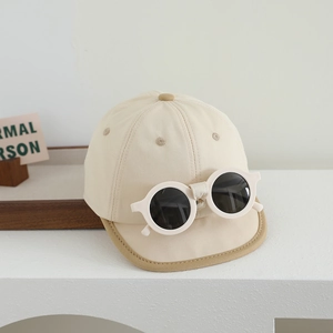 Détail de casquette bébé en coton beige avec lunettes de soleil rondes sur table blanche