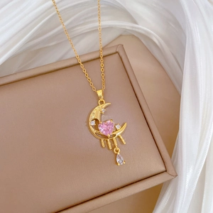 Macro shot of gold moon pendant with pink heart gemstone and sparkling water drop detail