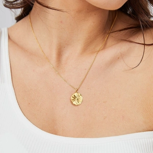 Close-up of golden stainless steel starburst pendant necklace worn by a fashion model