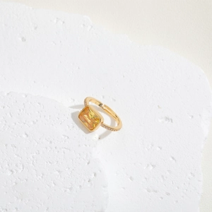 Detailed close-up of a gold ring with a yellow emerald-cut gemstone on a stone base