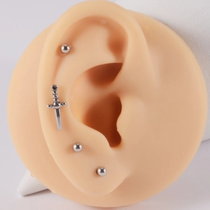 Close-up of silver sword and ball stud earrings on a silicone ear model display