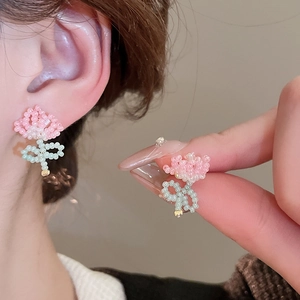 Handmade beaded flower stud earrings in pink and green, shown on a model for size