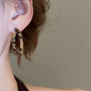 Close-up of leopard pattern C-shaped earrings with gold clasp on model's ear