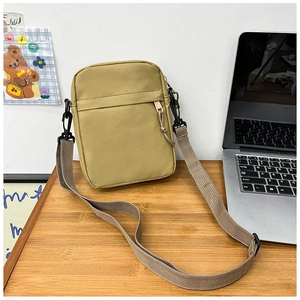 Detail view of the durable nylon fabric texture and front zipper pocket on a khaki cross-body bag