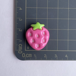 Detailed close-up of a pink resin strawberry charm on a centimeter grid mat showing its 2.5cm size