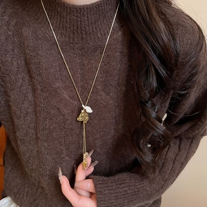 Detail view of a long gold tassel necklace with white flower petals on a brown sweater