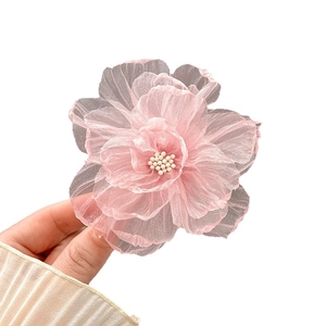 Pince à cheveux fleur en organza rose avec centre perlé, tenue à la main sur fond blanc