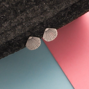 Close-up of shell-shaped stainless steel earrings with textured lines on a dark base