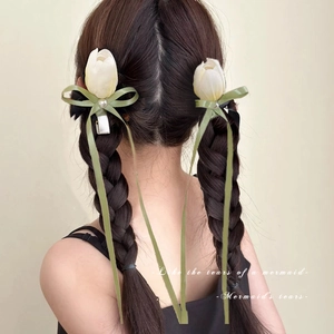 Detail of white tulip hair clips with green ribbons and pearls worn by a model