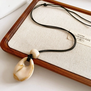 Detail of waterdrop resin pendant with amber texture on a black wax rope cord