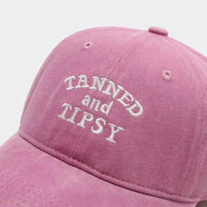 Dettaglio del ricamo bianco TANNED and TIPSY su cappellino in cotone rosa lavato