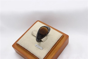 Macro detail of men's black ring featuring a round tiger eye stone on a wooden stand