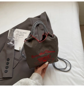 Detail of drawstring shoulder bag featuring red butterfly cherry embroidery and checkered strap