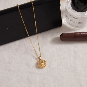 Detail of 18K gold stainless steel sun pendant necklace on elegant white fabric background
