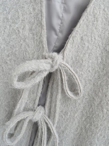 Detail van een lichtgrijze pluche jas met zachte imitatiebont textuur en vetersluiting