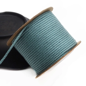 Detailed view of 1.5mm teal woven cotton cord wound on a brown paper spool for DIY crafts