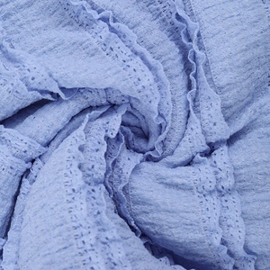 Macro shot of light blue fabric with intricate pleated textures and hollow-out details