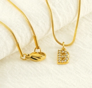 Detailed close-up of golden snake chain necklace with sparkling letter B pendant and lobster clasp