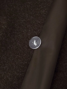 Close-up of brown wool fabric texture with transparent button and satin piping detail
