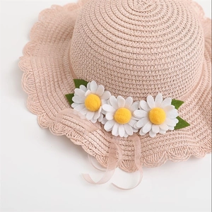 Close-up of pink woven straw hat with white daisy floral accents and wavy edge