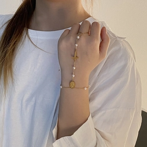 Detailed close-up of a golden finger bracelet with pearls and a religious cross charm