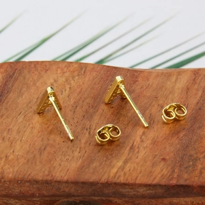 Macro shot of gold-plated letter A stud earrings with sparkling cubic zirconia on wood