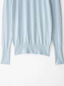 Detail showing high-quality light blue knit sweater hem with fine ribbed texture and cuffs