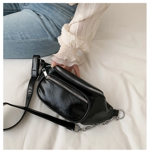 Detail of black glossy faux leather waist bag with silver chain and dual zippers