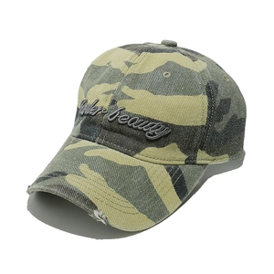 Detail of distressed camouflage baseball cap featuring Under Beauty script embroidery