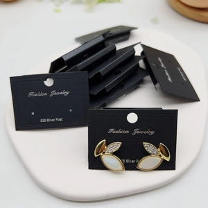 Leaf-shaped gold earrings with diamonds and white shells on a black jewelry card